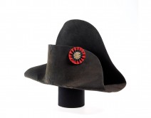 A black bicorne hat with a red, blue and white circular badge on the front