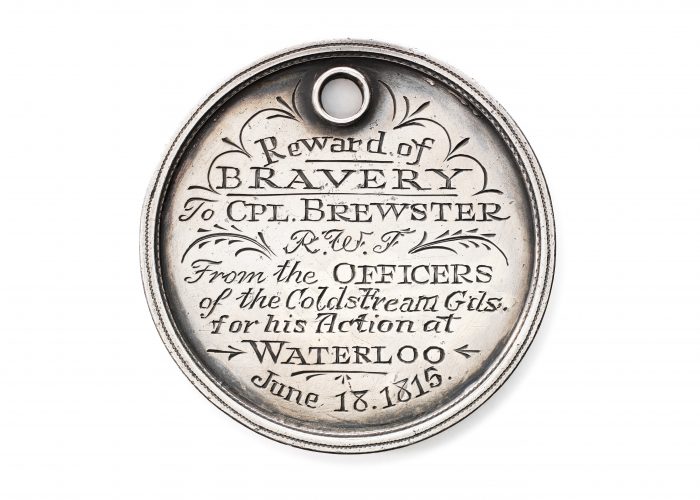 a photo of a silver medal with the inscription: Reward of Bravery to Cpl Brewster from the Officers of the Coldstream Gds for his action of Waterloo June 13, 1815.