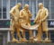 A photograph of a gold statue showing three men dressed in typical Victorian fashion discussing the plans for the railway