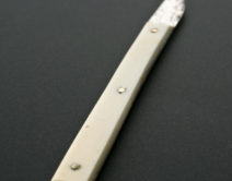 A long white handle with a small blade at one end and four sharp spikes at the other.