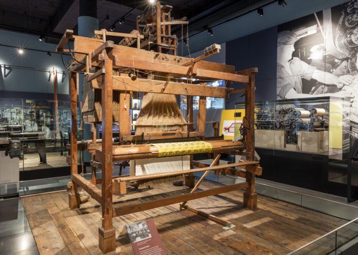 A photograph of a large wooden loom inside a museum building