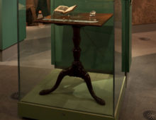 A photograph of the inside of the museum. A small wooden writing desk can be seen in a glass case.