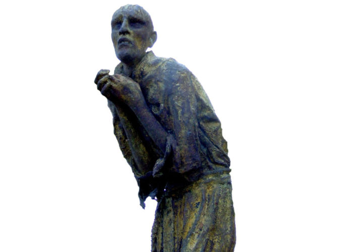 A photograph of a statue depicting a gaunt looking man, he is cowered over with his hands in a begging position and his eyes look sunken and scared.