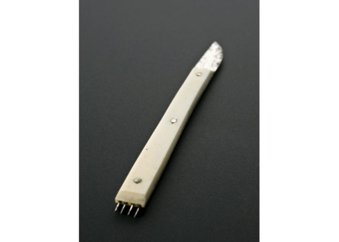 A long white handle with a small blade at one end and four sharp spikes at the other.