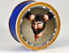 A photograph of a cylindrical pot, the face or lid of the pot has a painting of a dripping severed head held aloft by two hands. This is surrounded by the legend 'JEREMIAH BRANDRETH WHO WAS EXECUTED AT DERBY NOV.R th 7th 1817 FOR HIGH TREASON'.