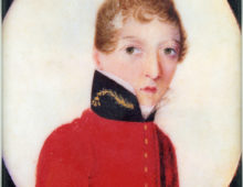 A miniature, oval portrait of a young soldier dressed in red military uniform and looking towards the viewer. The soldier has strawberry blonde curly but short hair