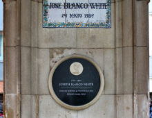 A photograph of a stone memorial with two plaques. At the top is a floral, tiled, blue and white plaque and beneath it is a circular black plaque. Both read the name 'Joseph Blanco White'