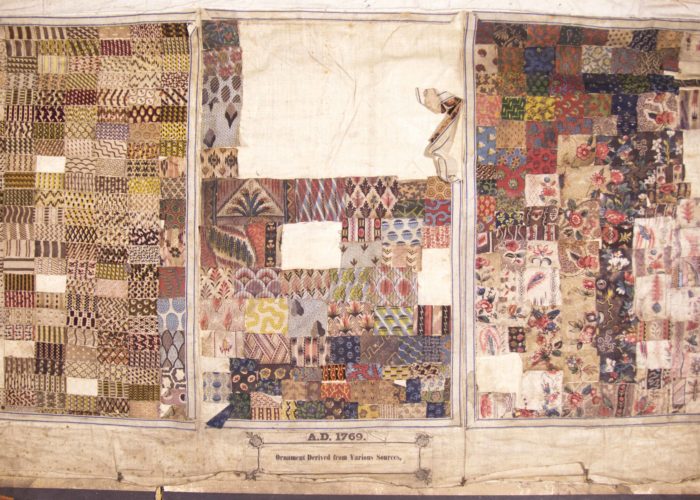 A photograph of the inside of a textile sample book. The worn parchment page is divided into three sections, each made up of little squares of different fabric patterns.