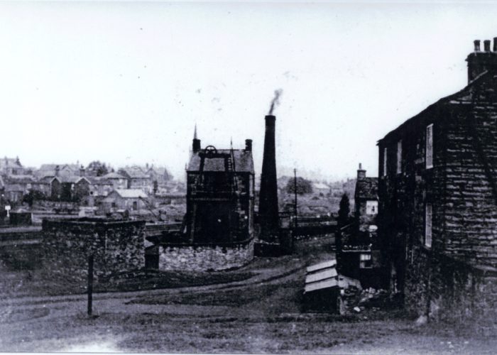A black and white photo of a small mill with a large brick chimney