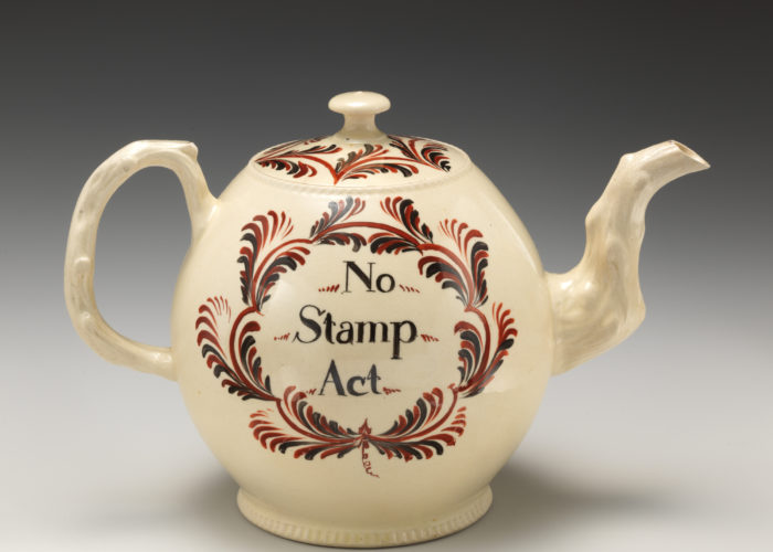 A photo of a white tea pot with red decoration and text that reads 'No Stamp Act'