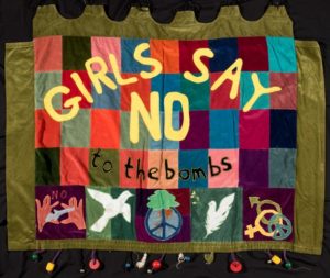 fabric banner with peace symbols reading 'girls say no to the bombs'