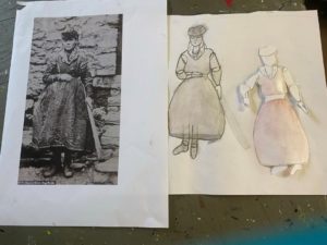 photo of person with voluminous skirt next to drawing and paper puppet of figure