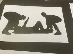 silhouette of two figures attending a figure lying on the ground